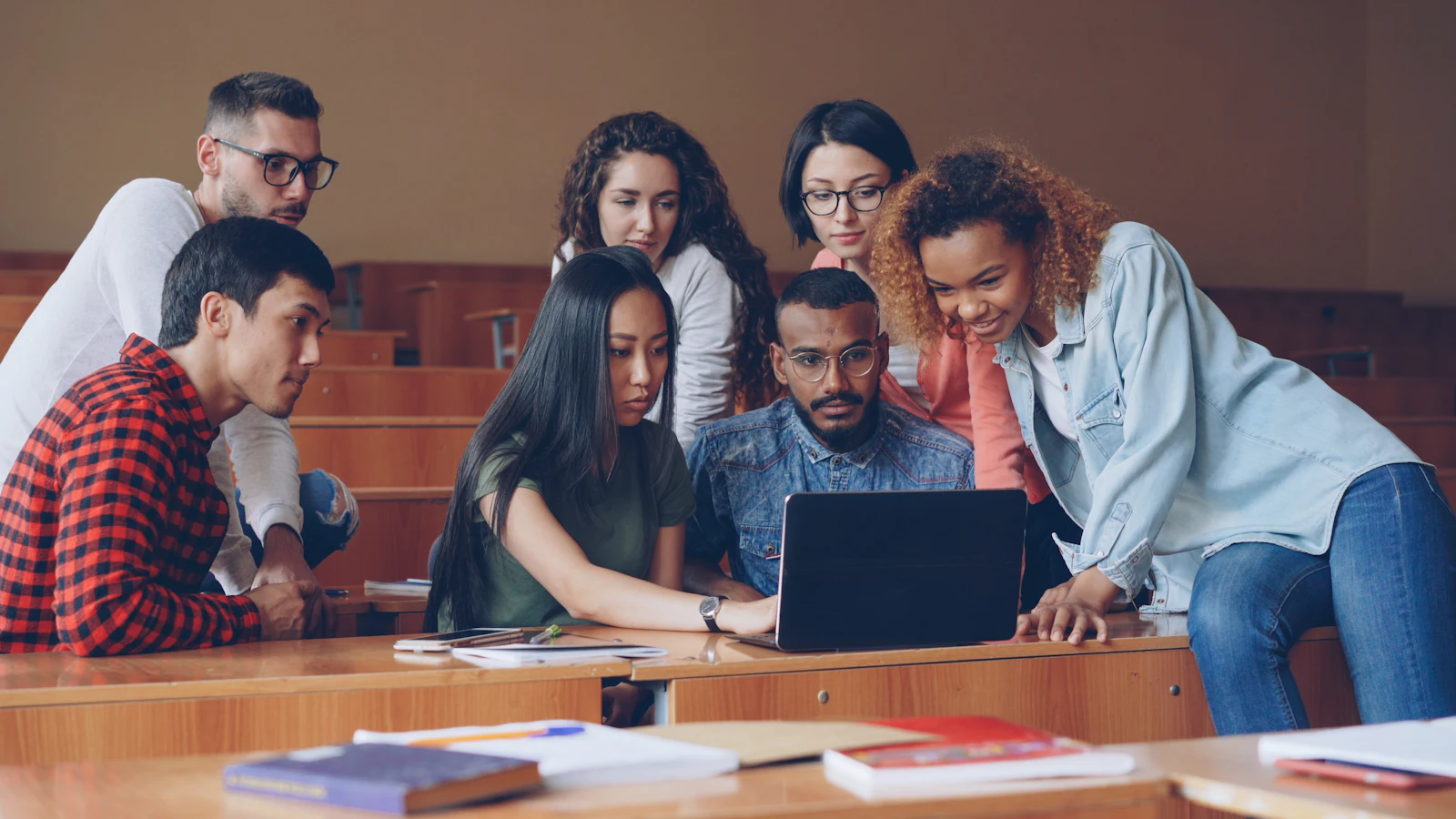 Students gathered around a laptop in a lecture hall.