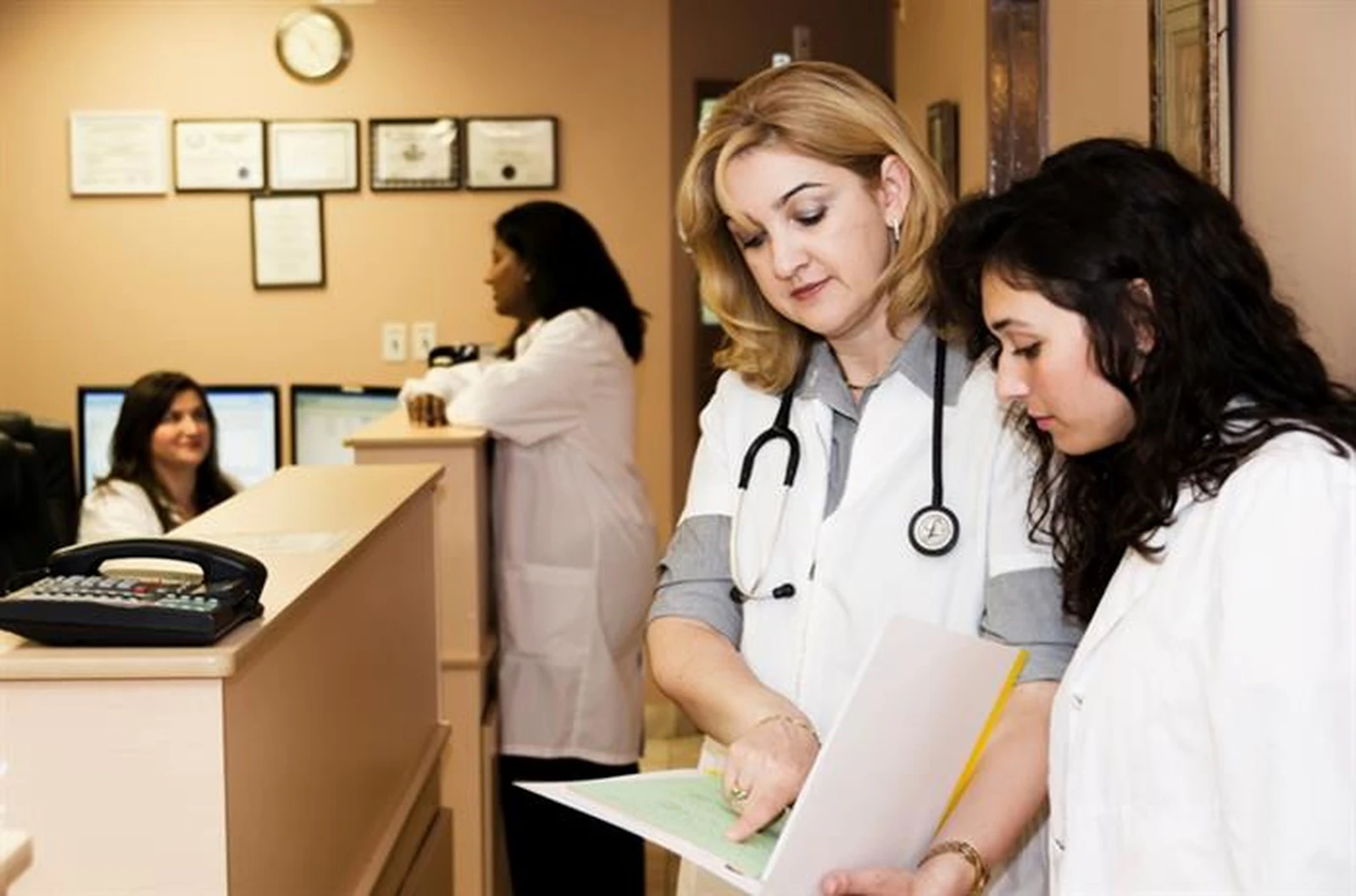 Two doctors reviewing a patient file at a clinic reception desk.