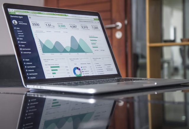 A laptop on a glass desk showing an analytics dashboard: traffic charts, channel breakdowns and headline numbers.