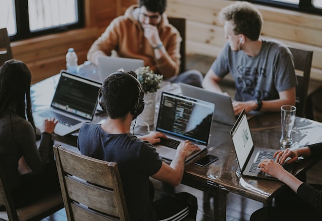 Four people working on laptops around a wooden table